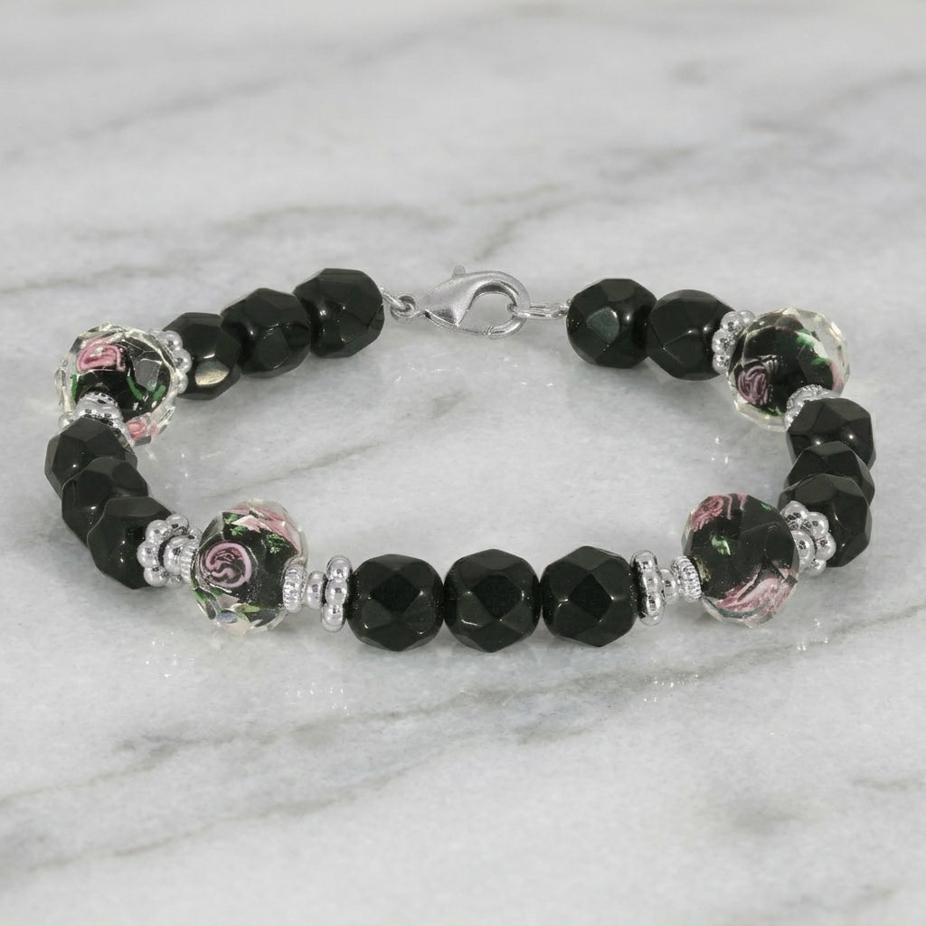 Black beaded bracelet with pink floral designs and silver tone metal resting on a marble surface