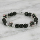 Black beaded bracelet with pink floral designs and silver tone metal resting on a marble surface