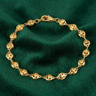 Gold tone happy face bracelet with a lobster clasp closure resting on dark green fabric
