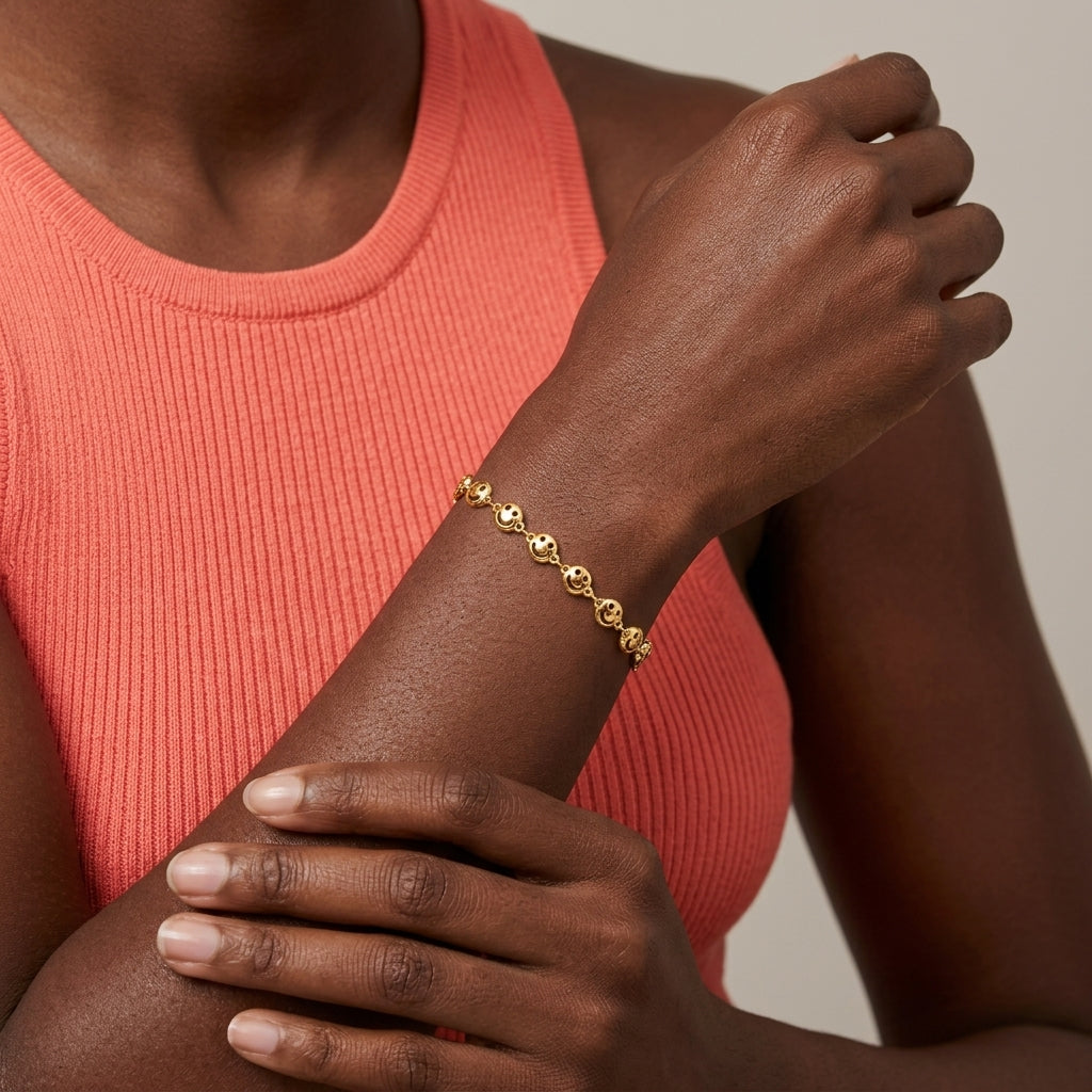 Woman in a salmon pink top wearing a gold tone happy face bracelet on her wrist