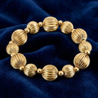 Round gold tone beaded bracelet resting on dark blue fabric