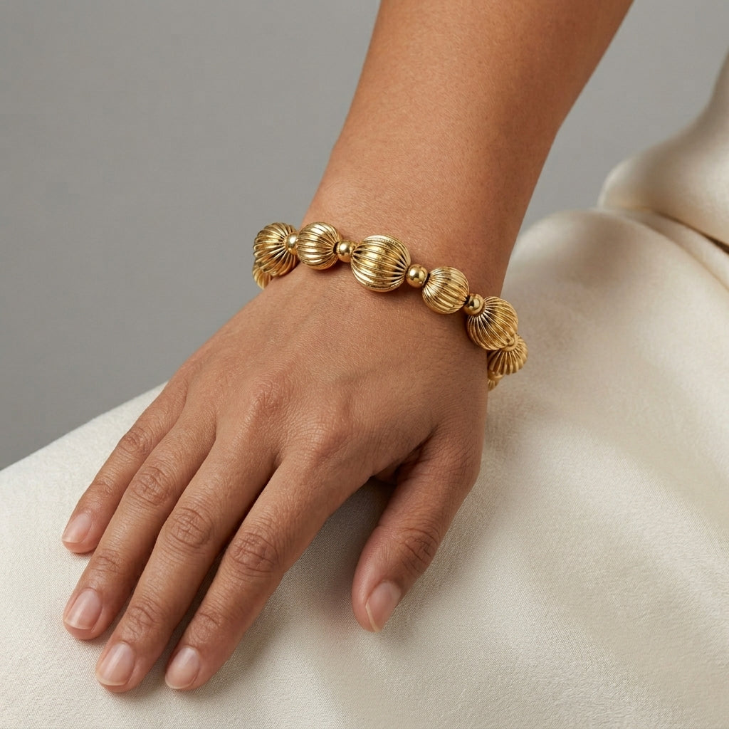 Woman wearing a round gold tone beaded bracelet on her wrist