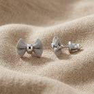 Petite Mesh Bow Stud Earrings resting on tan linen