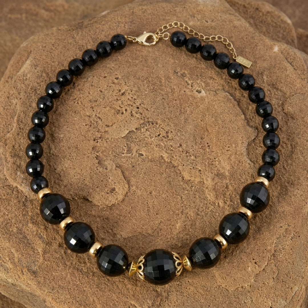 Round Black Faceted Beaded Stranded Necklace resting on a brown stone surface