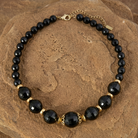 Round Black Faceted Beaded Stranded Necklace resting on a brown stone surface