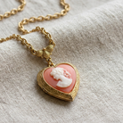 Gold tone necklace with a heart-shaped pink cameo pendant against a textured fabric background
