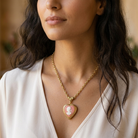 Woman wearing a gold tone necklace with a heart-shaped pink cameo pendant.