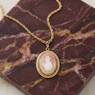 Gold tone necklace that has a carnelian ivory cameo pendant resting on a slab of dark red marble