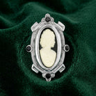 Black cameo brooch with black crystal accents and a silver tone frame resting on dark green fabric