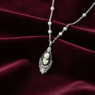 Silver tone chain necklace with a black cameo pendant and white faux pearls on the chain resting on dark red fabric