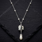 Three cameo spinner pendant necklace with white faux pearls resting on dark stone surface