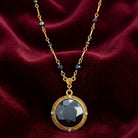 Round Faceted Hematite Glass Stone Pendant Necklace resting on dark red fabric
