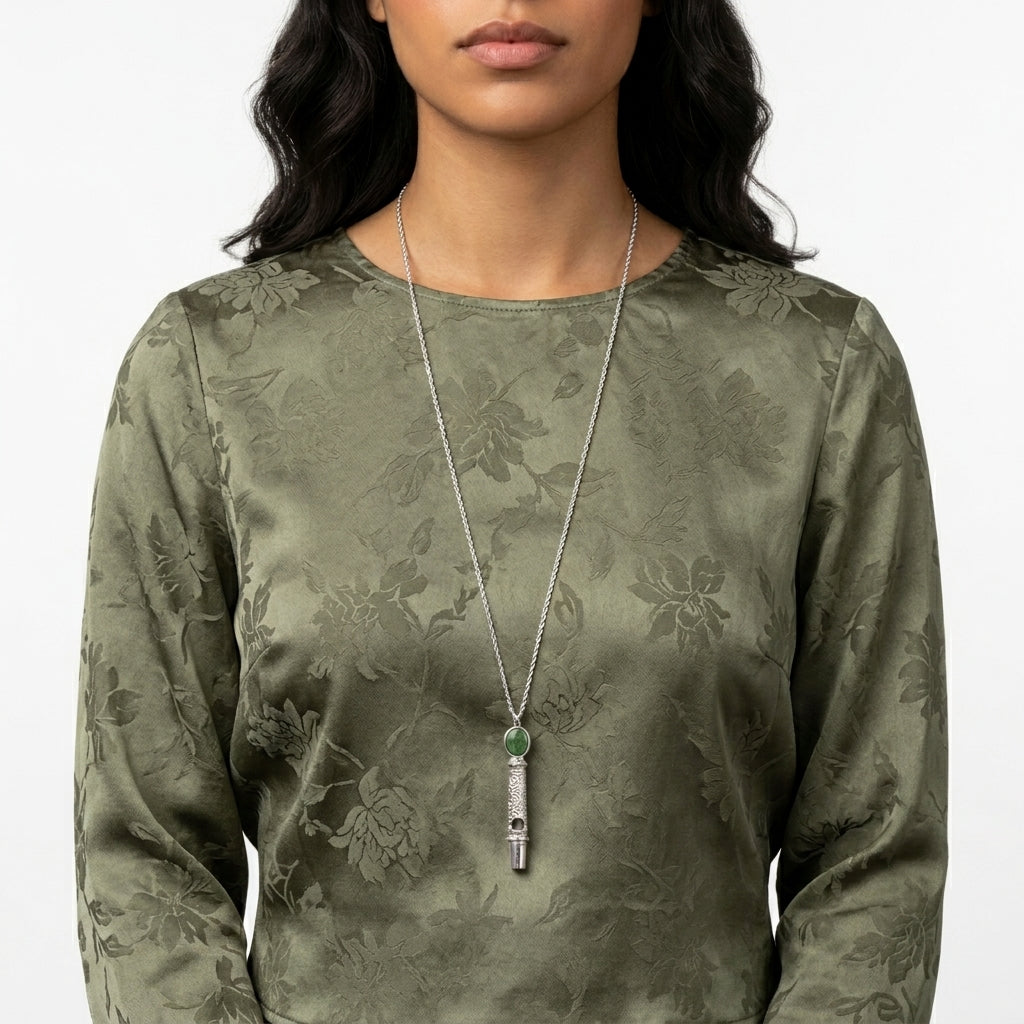 Woman in a floral green long sleeve outfit wearing our Oval Jade Gemstone Filigree Whistle Pendant Necklace
