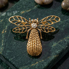 Gold tone bee brooch pin with crystal accents resting on a dark green marble surface