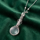 Pewter Golf Club Set Magnifier Pendant Necklace resting on green fabric