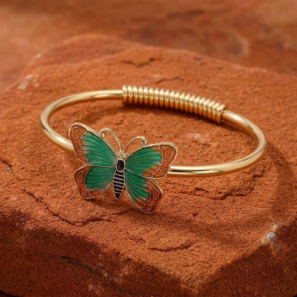 Green butterfly bracelet on a gold tone spring hinge resting on red sandstone