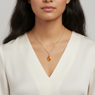 Woman wearing a necklace with a topaz crystal pendant, as well as two charms: one faux pearl and the other an amber-colored heart. All against a neutral background.