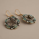Pair of ornate peacock plumage wreath lever back earrings with AB crystals on a beige background