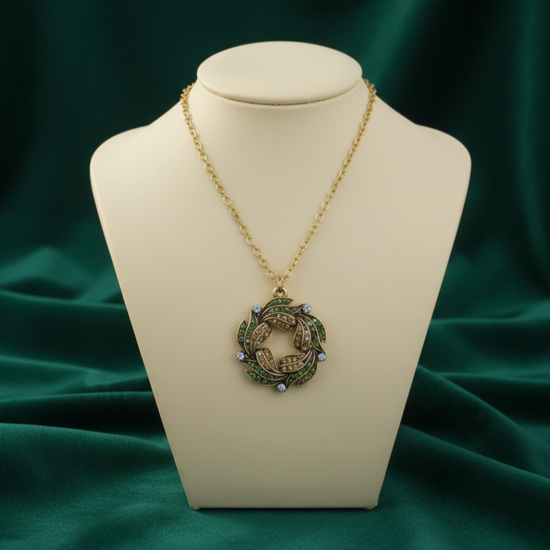 Gold necklace with a green Peacock feather wreath pendant on a mannequin bust against a green fabric background.