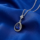 Atlantic Blue Stone Teardrop Crystal Pendant Necklace resting on dark blue satin fabric surface