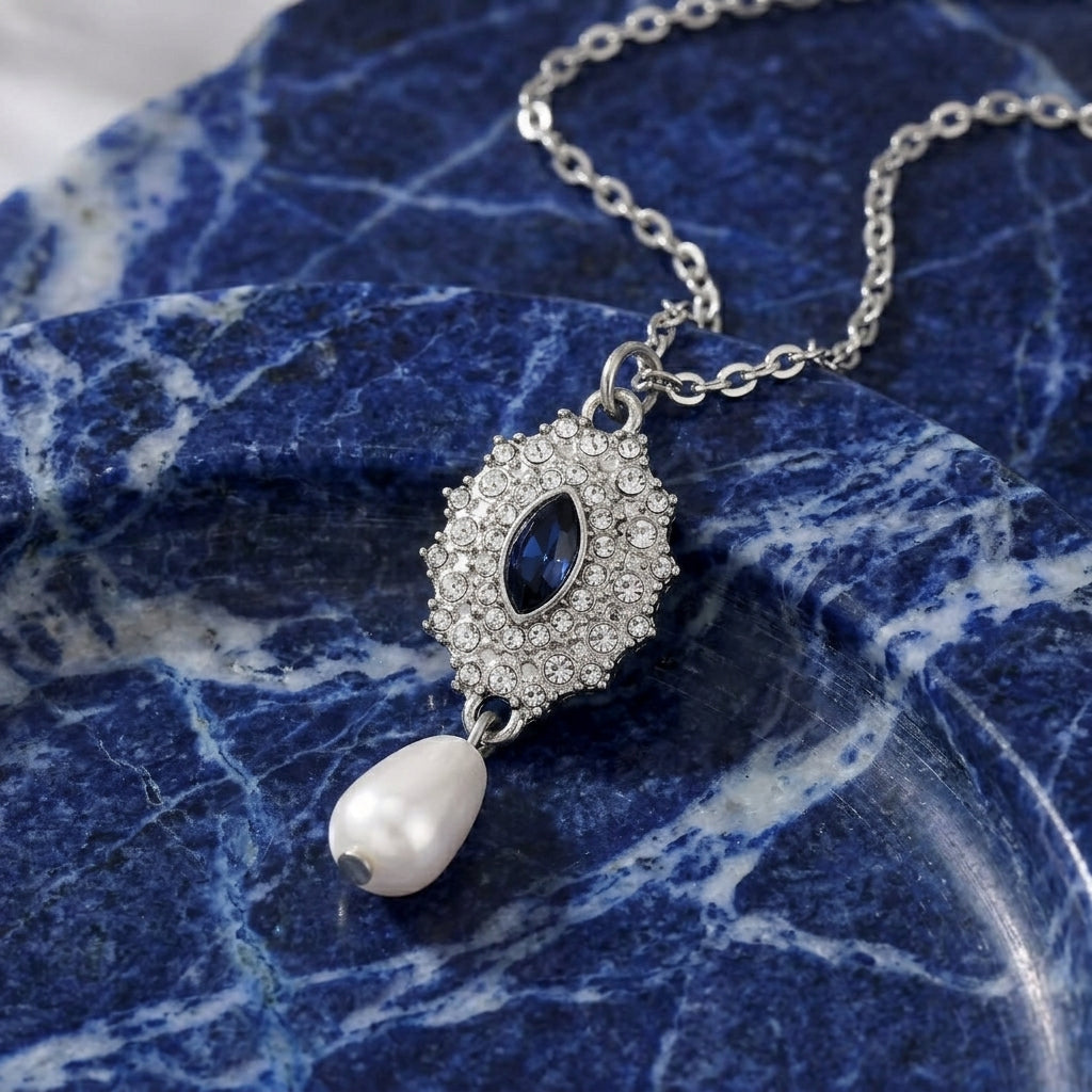  Blue crystal Starburst Crystal Faux Pearl Drop Pendant Necklace laying on a blue marble stone surface