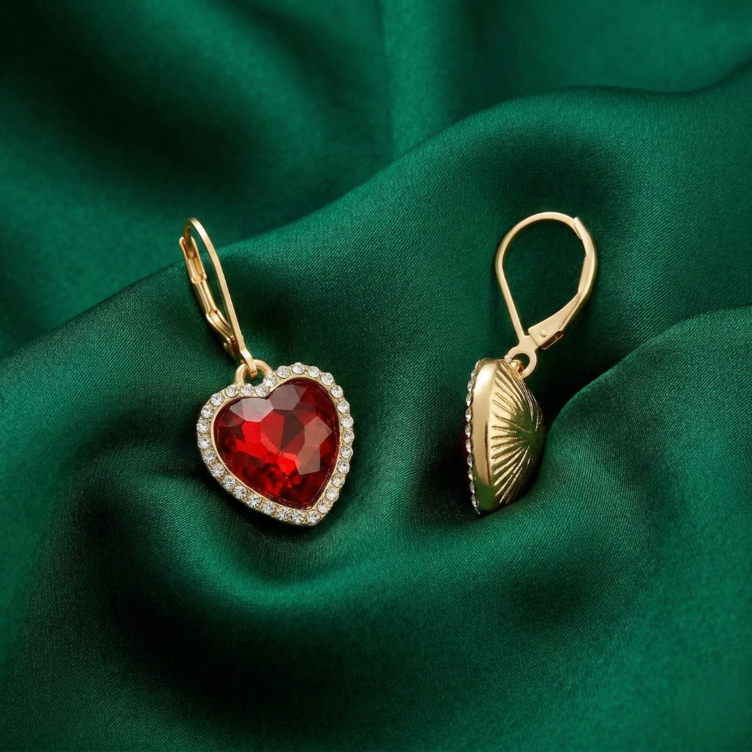 Gold earrings with red heart-shaped crystals on a green fabric background