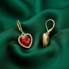 Gold earrings with red heart-shaped crystals on a green fabric background