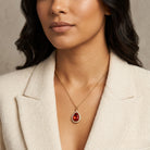 Woman in a cream blazer wearing a gold tone red teardrop crystal pendant necklace with crystal accents