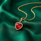 Heart-shaped red pendant on a gold chain against a green fabric background