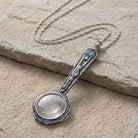 Blue crystal magnifying glass pendant necklace resting on a stone surface