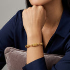 Gold colored beaded bracelet worn by a woman with a blue shirt