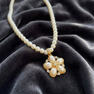 White faux pearl necklace with a floral pendant design and crystal accents resting on a dark gray fabric surface