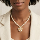Woman in a white blazer wearing a white faux pearl necklace with a floral pendant design