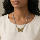 Woman wearing a necklace with a butterfly pendant on a neutral background