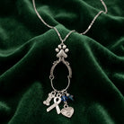 Silver tone charm necklace that as four distinct pet rescue-inspired charms laying on dark green fabric