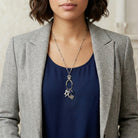 Woman in a gray blazer and a blue shirt wearing a silver tone charm necklace that as four distinct pet rescue-inspired charms