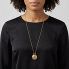 Woman wearing a black top with a gold tone necklace that has a locket pendant featuring a peridot green crystal
