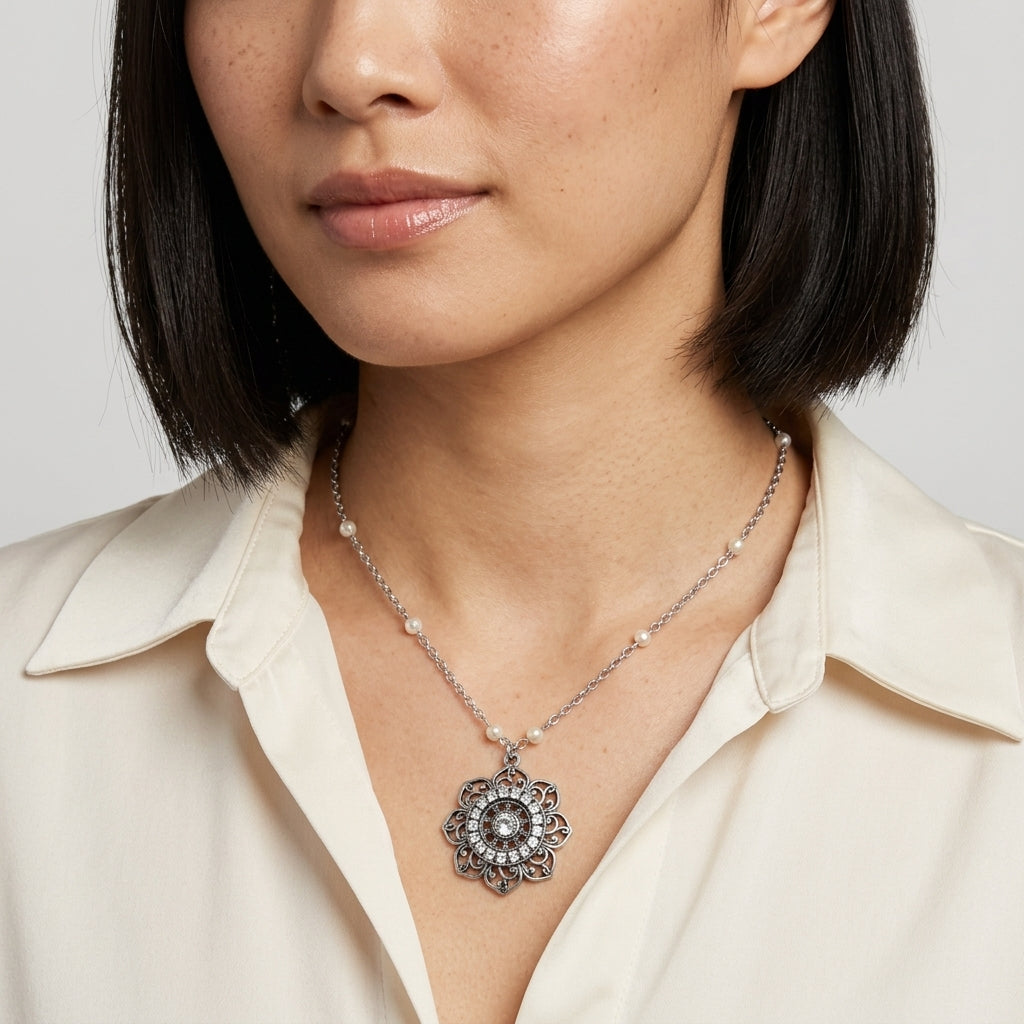 Woman wearing a cream top with a silver tone floral pendant necklace that has clear crystal accents and white faux pearls on the chain