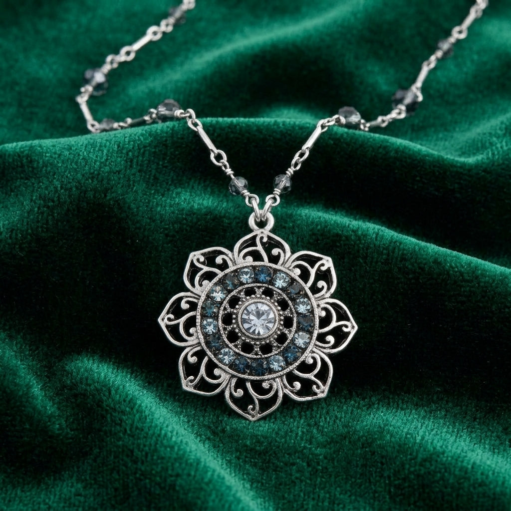 Silver tone floral pendant necklace that has blue beads and crystals resting on dark green satin fabric