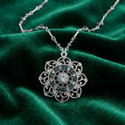 Silver tone floral pendant necklace that has blue beads and crystals resting on dark green satin fabric