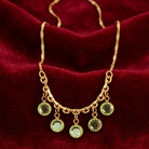 Gold tone necklace that has dangling green Austrian channel crystals resting on red fabric