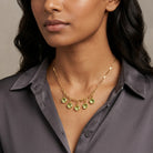 Woman in a dark blouse wearing a gold tone necklace that has dangling green Austrian channel crystals