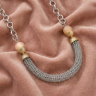 Beige moonstone necklace that has silver tone tube and mesh chains resting on light pink fabric