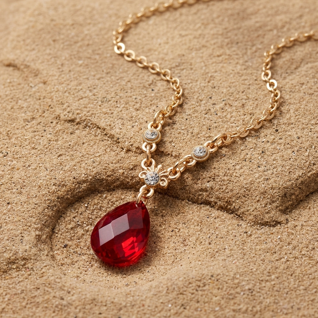 Red teardrop pendant necklace with crystal accents resting on a sandstone surface