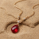 Red teardrop pendant necklace with crystal accents resting on a sandstone surface