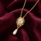 White faux pearl drop pendant with a floral design resting on dark red fabric