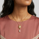 Woman in a muted dark pink top wearing a faux pear drop pendant necklace with a floral design
