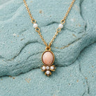 Oval pink stone pendant necklace with white faux pearls resting on a blue stone surface