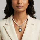 Woman wearing a faux pearl necklace with a cameo pendant against a neutral background