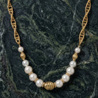 Pearl necklace with gold accents on a dark green marble background